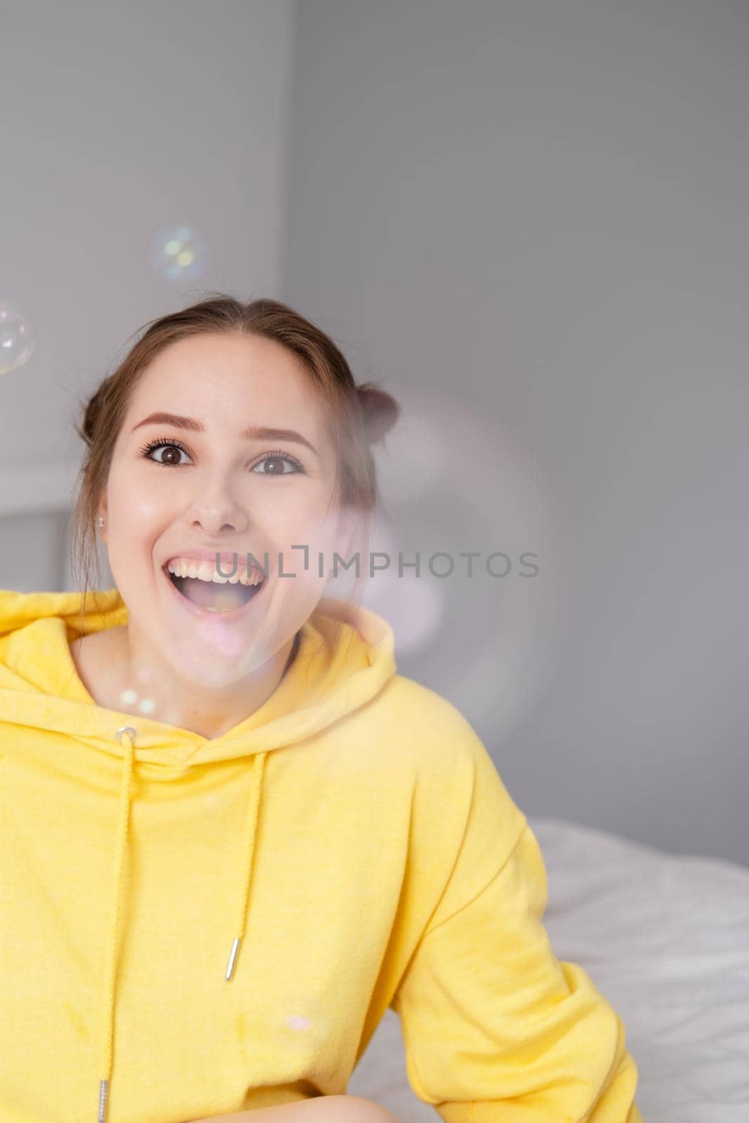 portrait of charming young woman in yellow among soap bubbles on bright grey background. fashionable teenager. trendy colours. by oliavesna