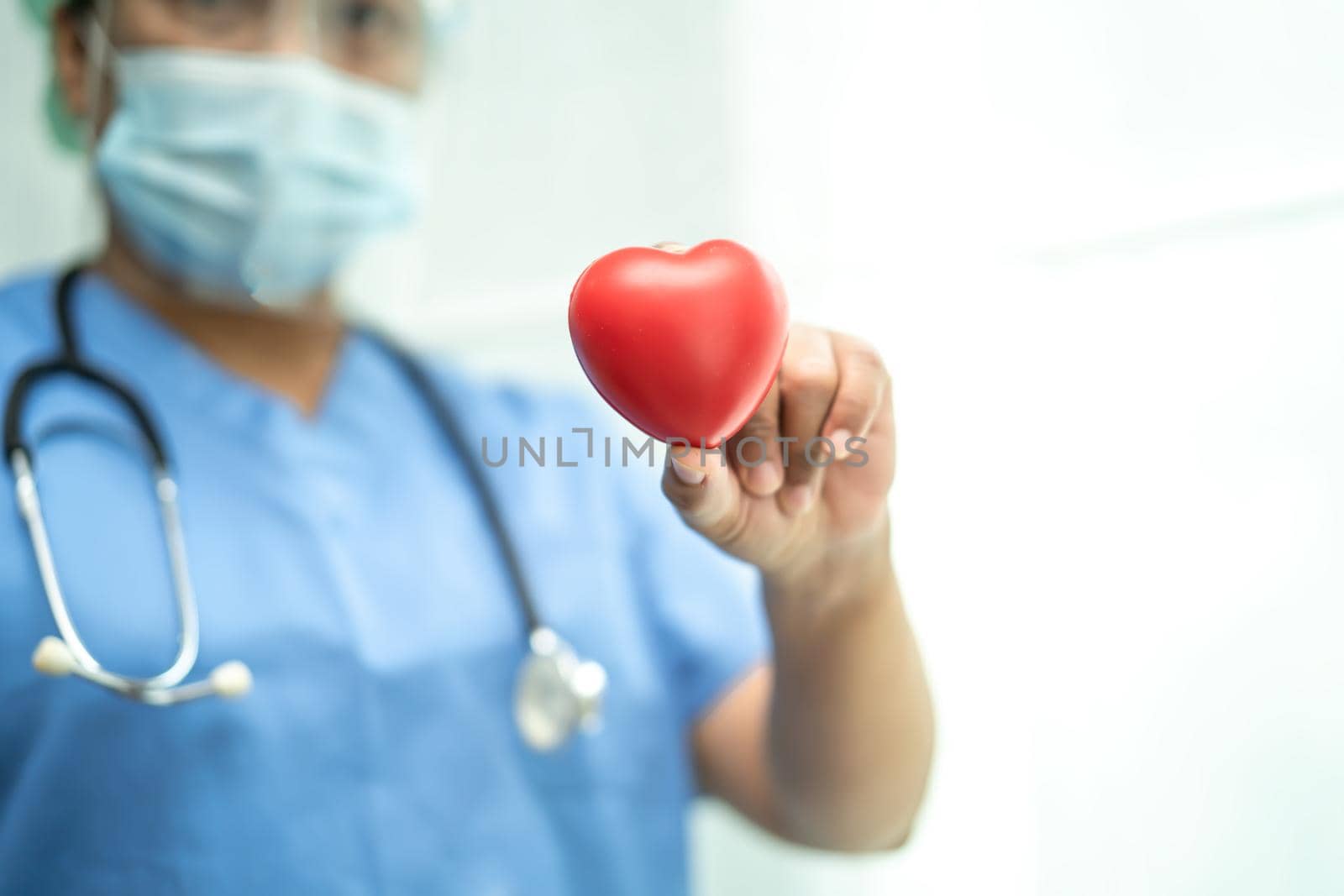 Asian doctor wearing face shield and PPE suit new normal to protect safety infection Covid-19 Coronavirus holding red heart in hand at hospital. by pamai