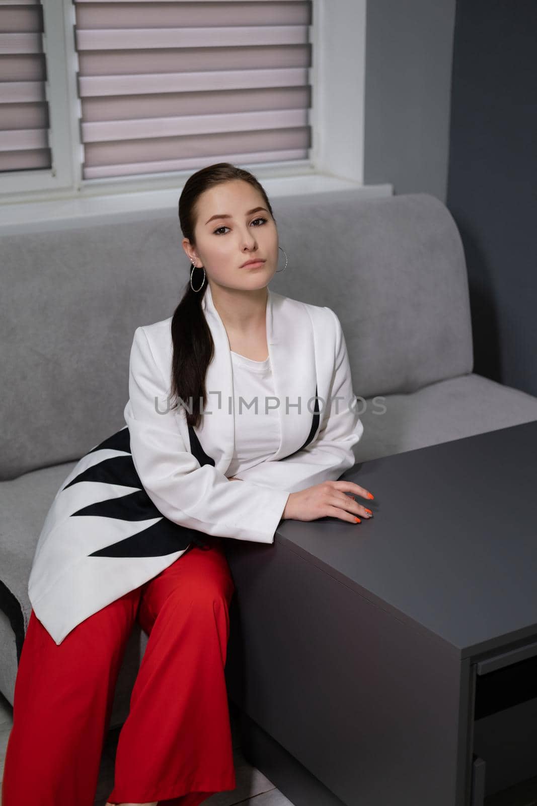 sexy business woman sitting by the table on couch in grey room - office. big boss. important, confident women. femininity. millennials.