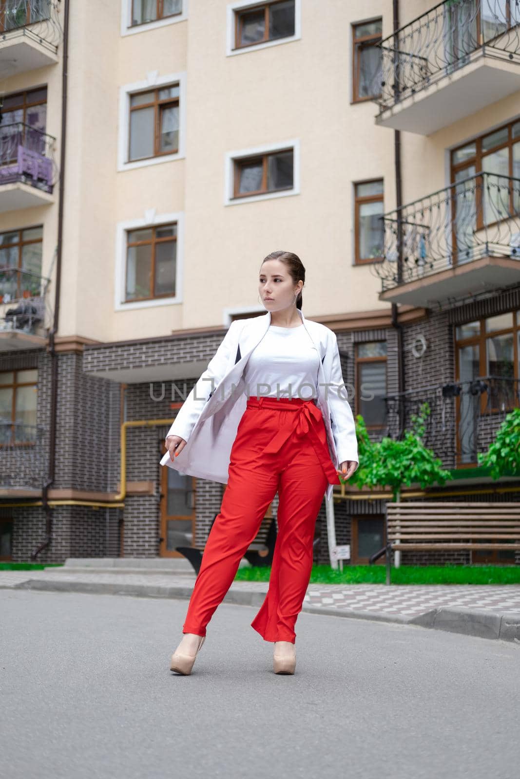 business woman in red pants, white blouse and jacket walking by the street by oliavesna