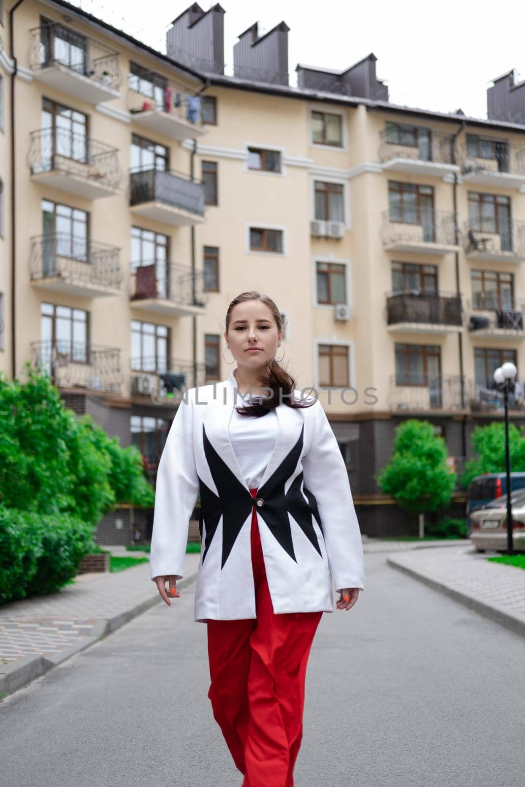 confident brunette woman in red pants and white blouse and jacket walking in the street by oliavesna