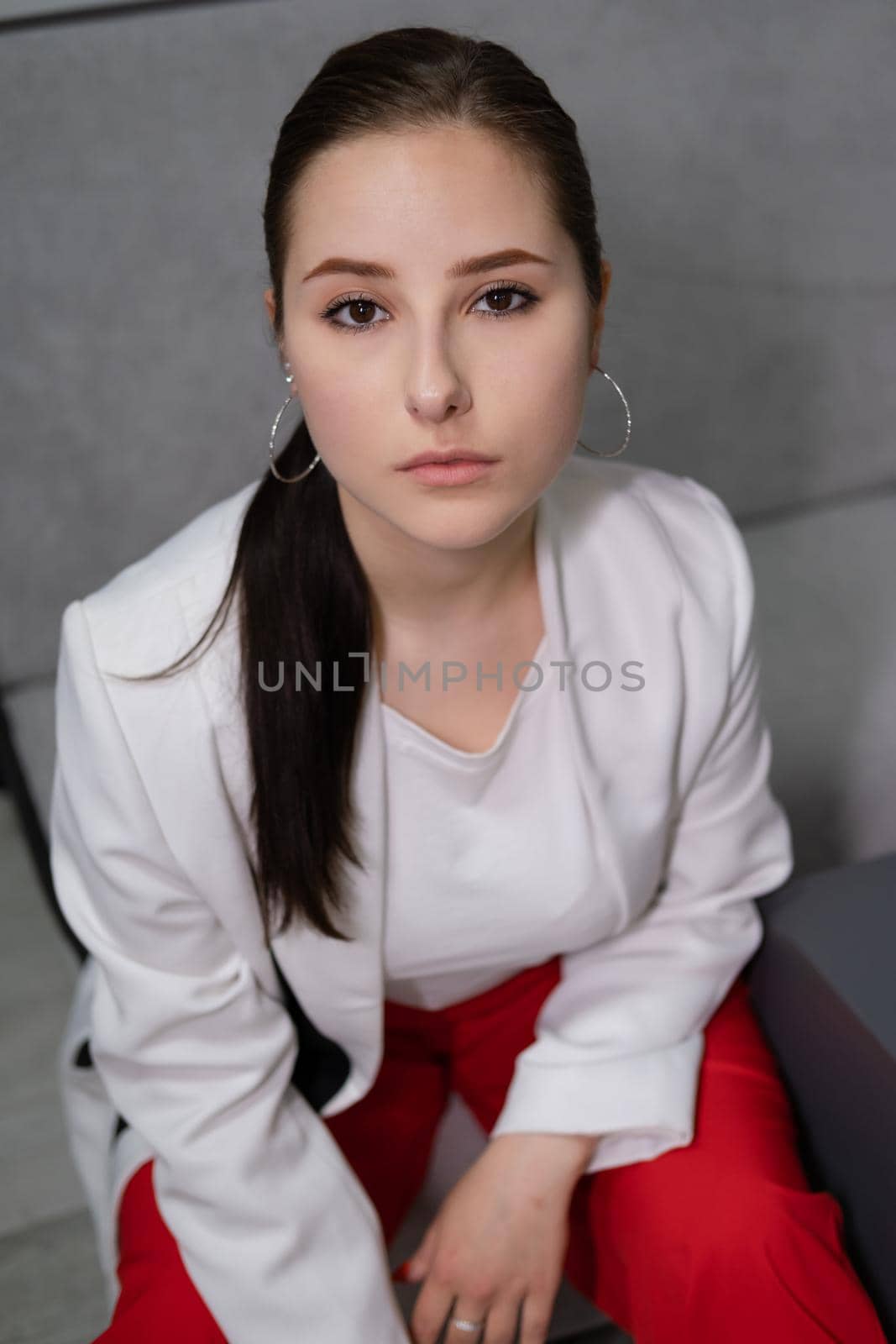 beautiful business woman in red pants, white blouse and Blazer sitting by the table on couch in grey room office by oliavesna