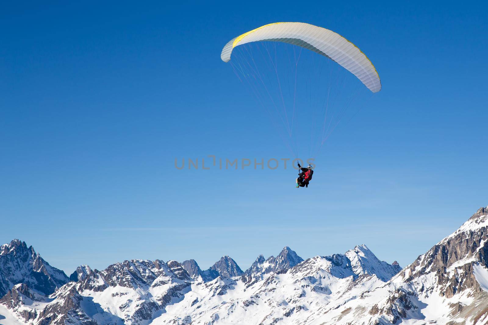 two people paragliding in tandem high in the blue sky