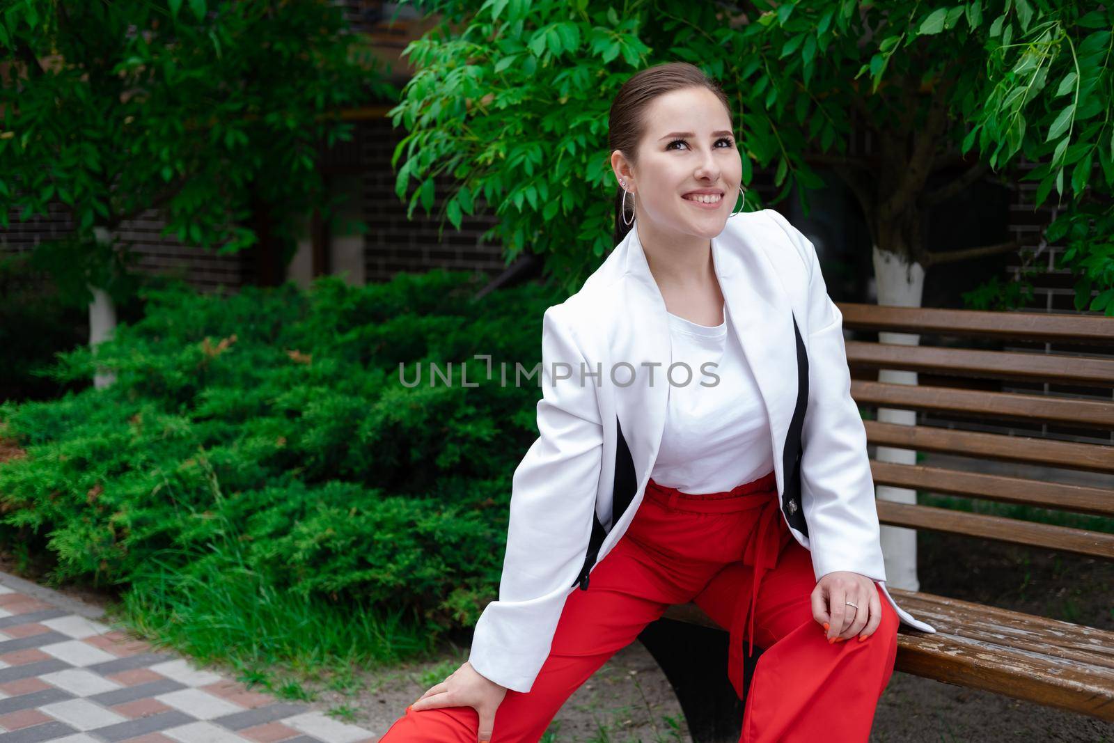 charming young brunette woman in red and white posing outdoors. summertime, green trees.