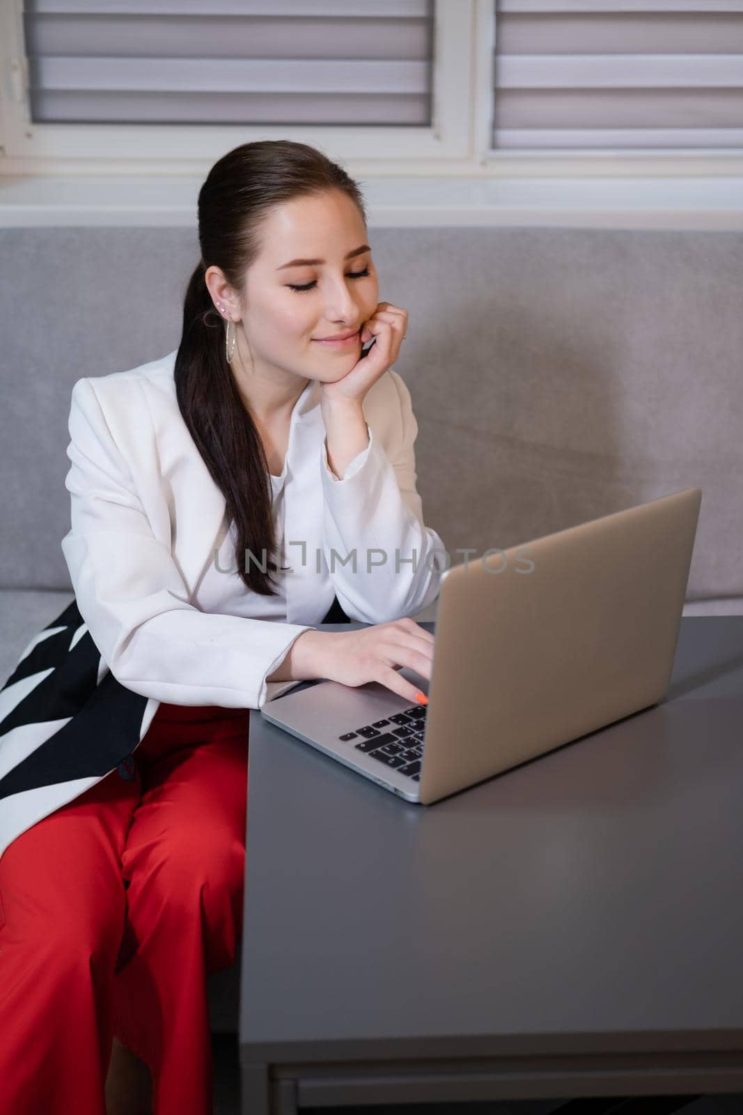 woman sitting by the table on couch in grey room - office and use laptop. big boss. important, confident women. femininity. millennials by oliavesna