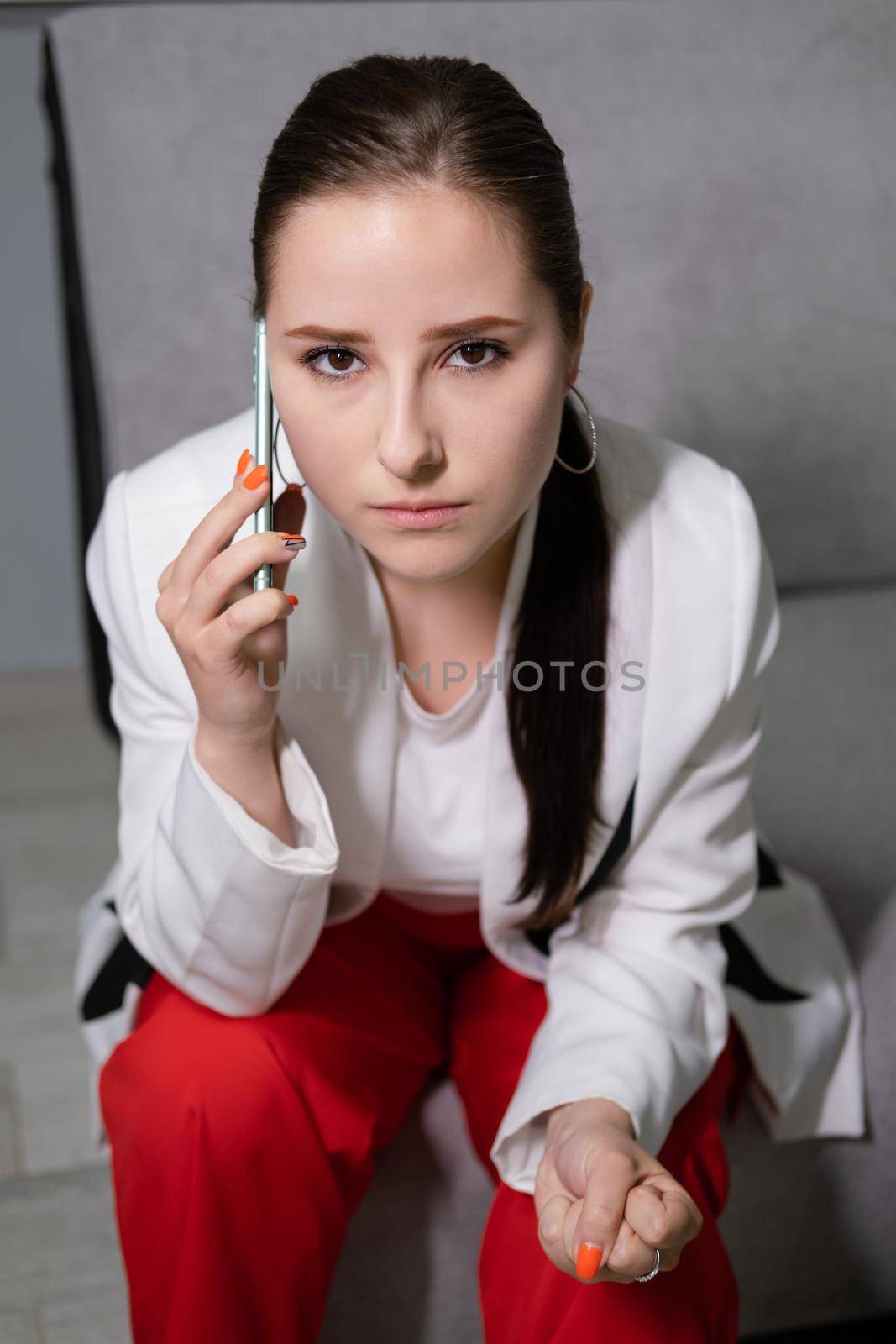 portrait of upset, angry and sad brunette business woman talking by phone in grey office. disturbing, bad phone call. problems, troubles by oliavesna