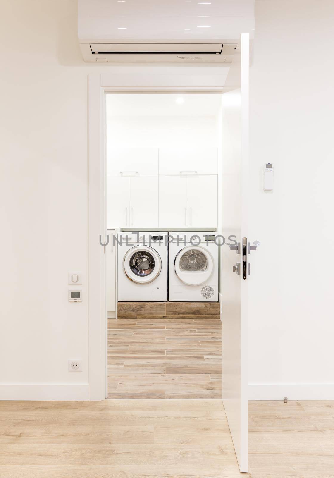 White opened door in modern home with air conditioner and wooden floor