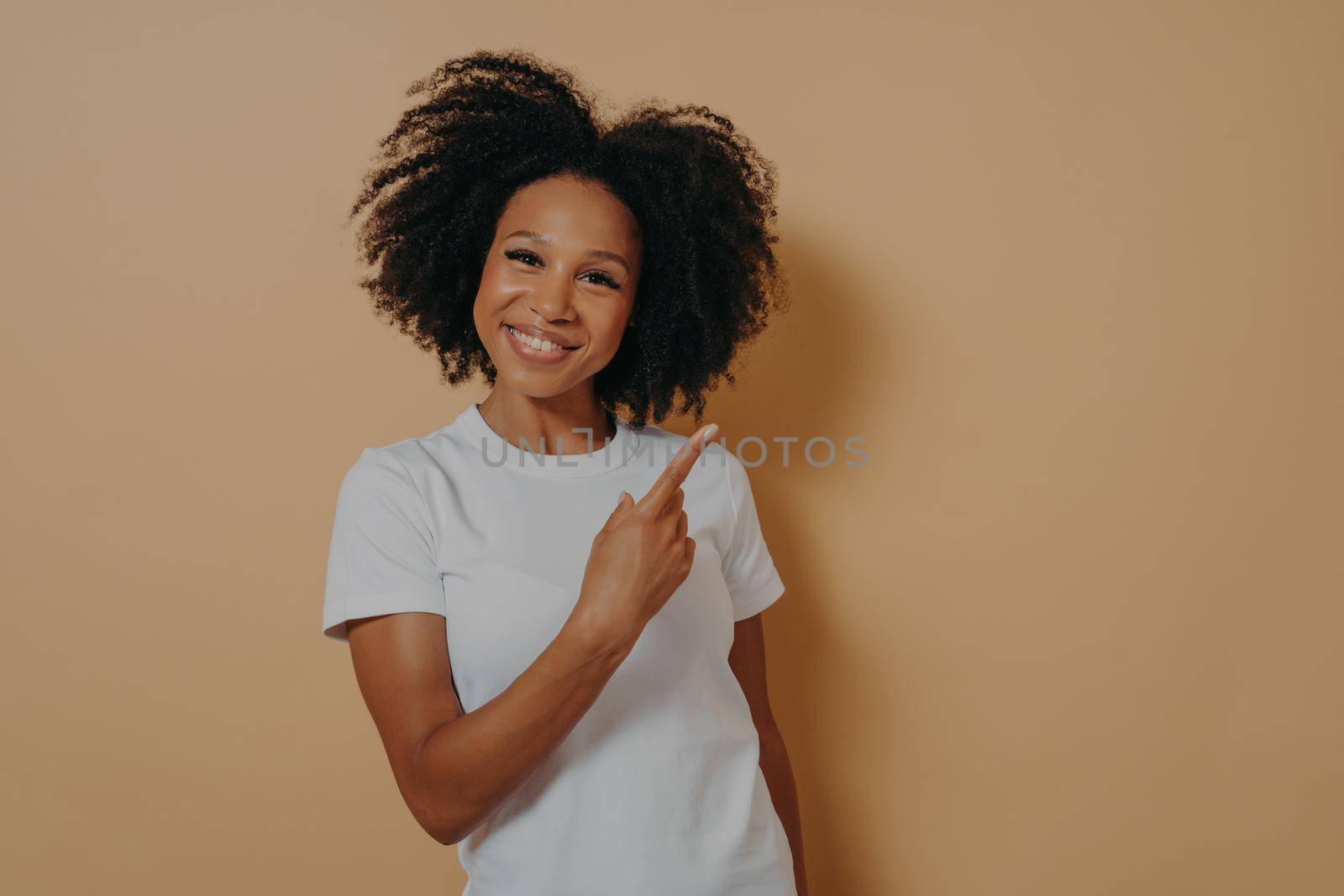 Positive young african female model in white shirt indicating with forefinger at blank copy space by vkstock