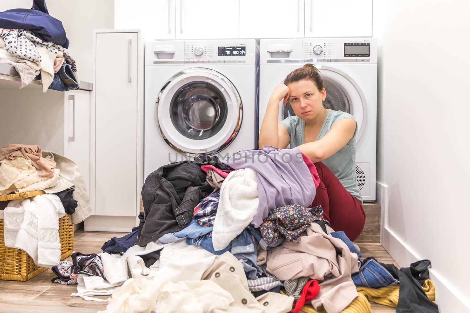 Sad woman sitting in laudry room with a pile of dirty clothes