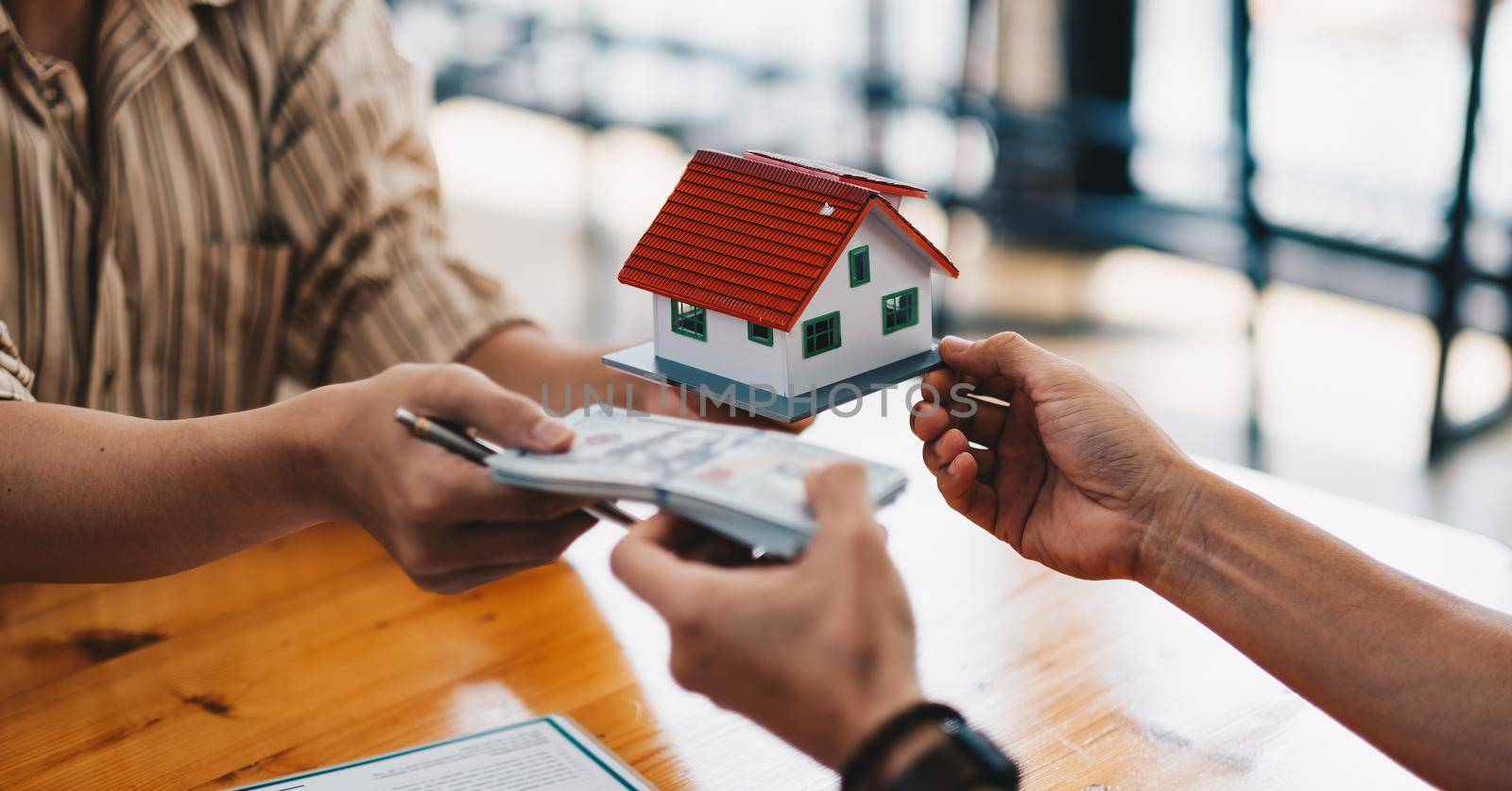 Close up of hands giving house model to other hands with money. Concept of real estate and deal