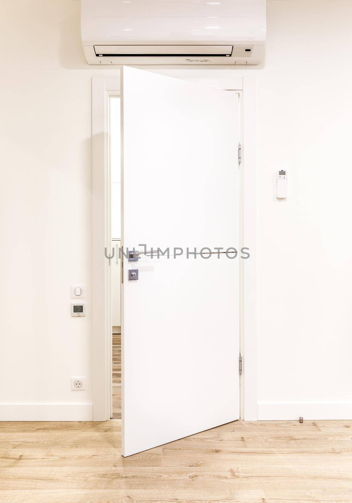 White opened door in modern home with air conditioner and wooden floor