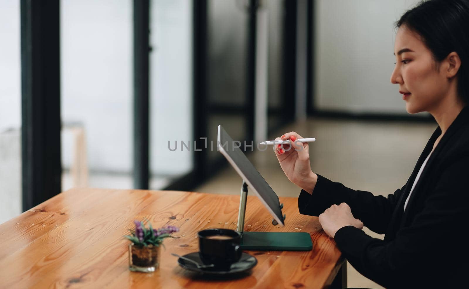 Side view of business woman holding stylus pen pointing on screen of digital tablet on wooden desk.