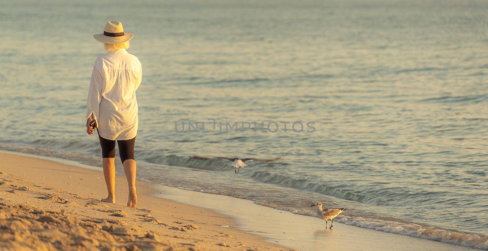 Woman wearing straw hat walking on beach at sunset