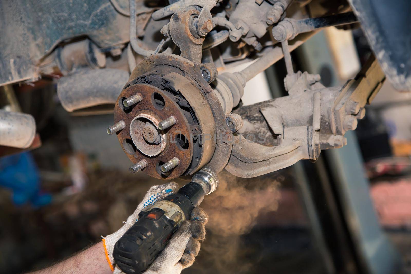 Gloved hands use a power tool to clean the rust on the rear wheel hub. In the garage, a man changes parts on a vehicle. Small business concept, car repair and maintenance service. UHD 4K.