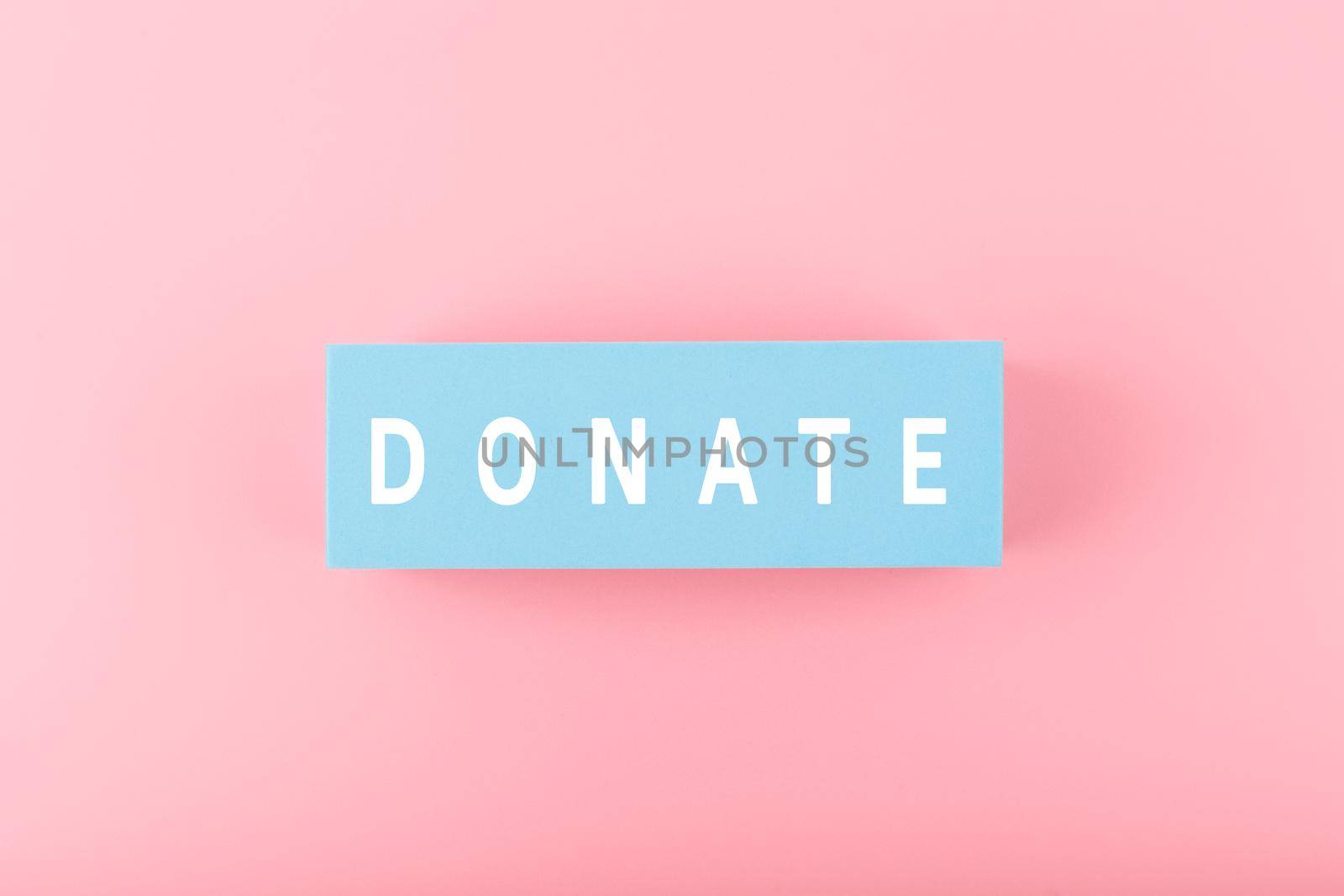 Donation or charity modern minimal concept. Single word donate written on light blue block against bright pink background. 
