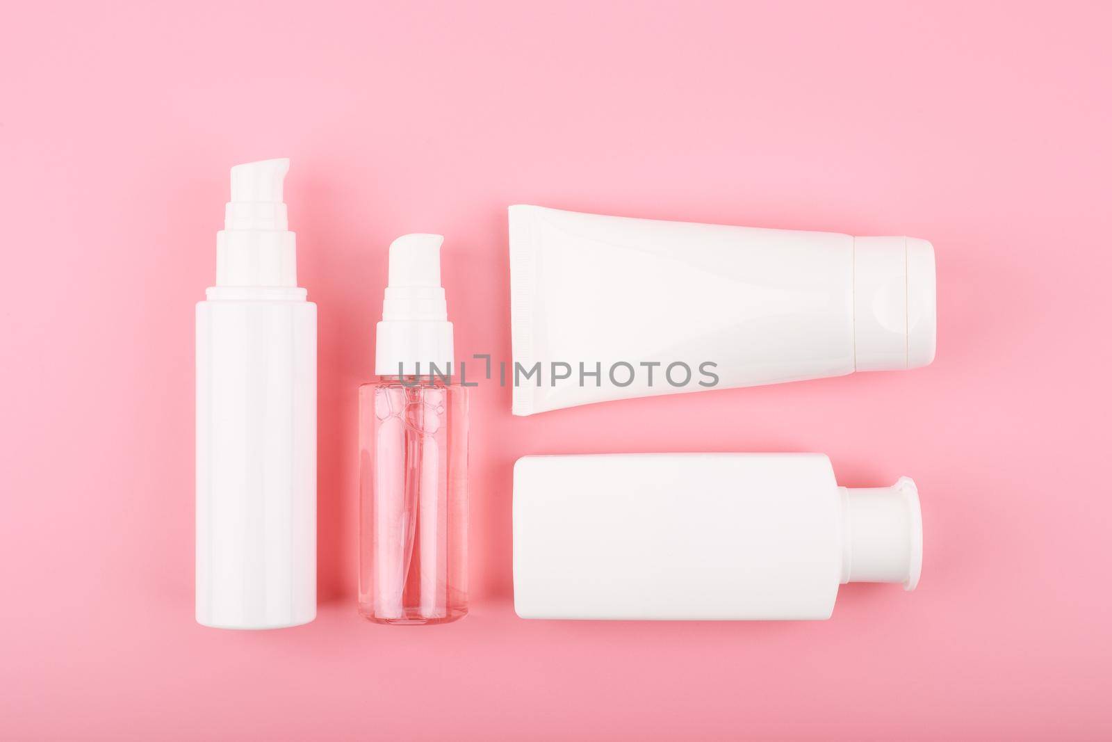 Set of cosmetic bottles for face cleansing, exfoliating, hydrating and anti aging treatment against pink background. Trendy modern flat lay with a set of beauty products for daily use 