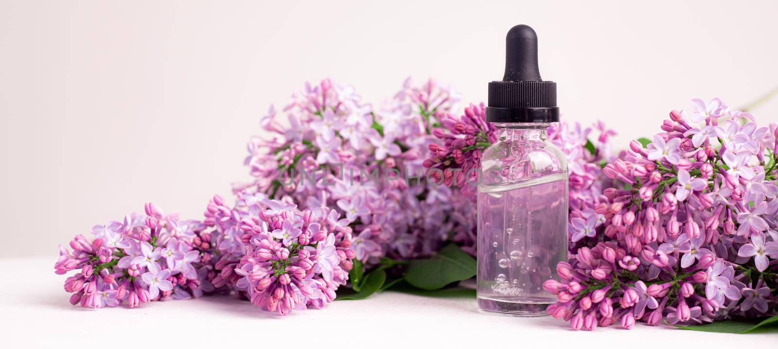 Hyaluronic acid bottle and lilac on a white background . Beauty container. Skin care. Vitamins for the skin. Rejuvenation. Female beauty. An article about the benefits of hyaluronic acid. Article about the choice of hyaluronate. Copy space. A branch of lilac. Flowering . Nature