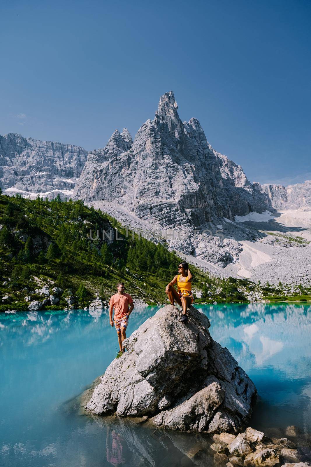 Morning with clear sky on Lago di Sorapis in the Italian Dolomites, milky blue lake Lago di Sorapis, Lake Sorapis, Dolomites, Italy. Couple man and woman mid age walking by the lake in the mountains 