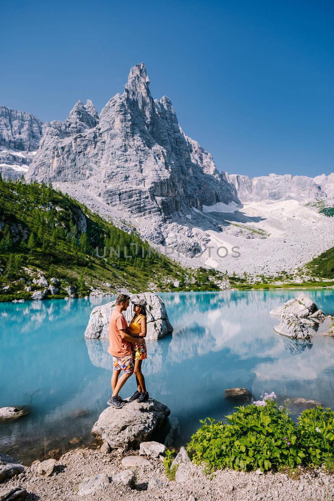 Morning with clear sky on Lago di Sorapis in the Italian Dolomites, milky blue lake Lago di Sorapis, Lake Sorapis, Dolomites, Italy. Couple man and woman mid age walking by the lake in the mountains 