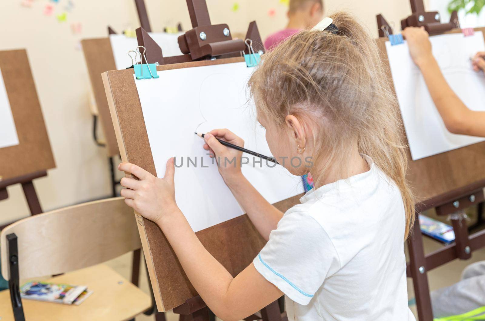 Little girl painting picture on easel in classroom