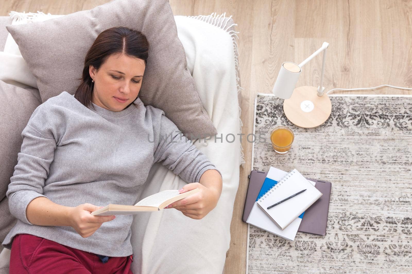 Young woman reading a book as she relaxes on her back on a comfortable sofa, view from above