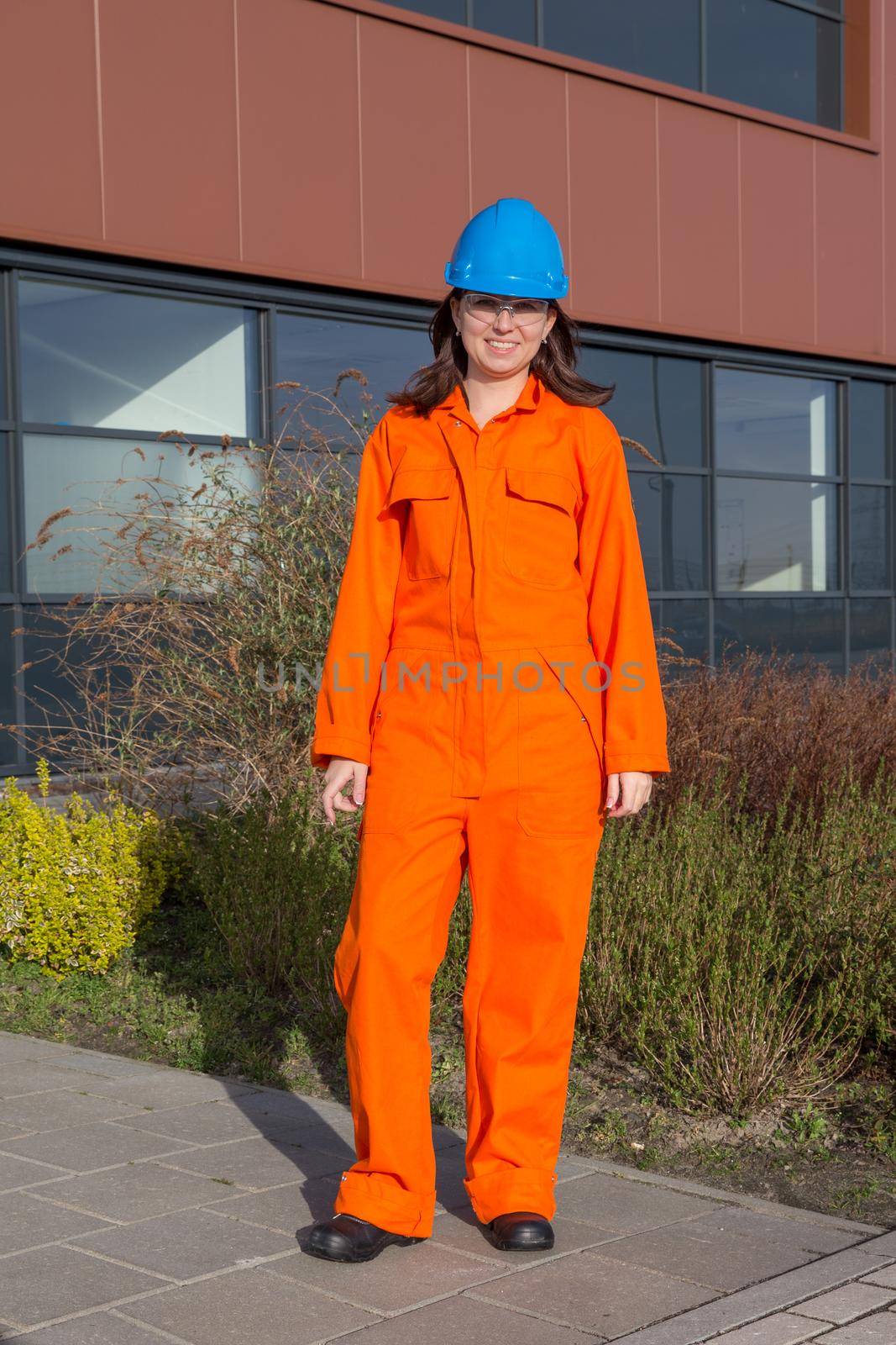 Woman worker in orange overall and blue safety helmet isolated on white background