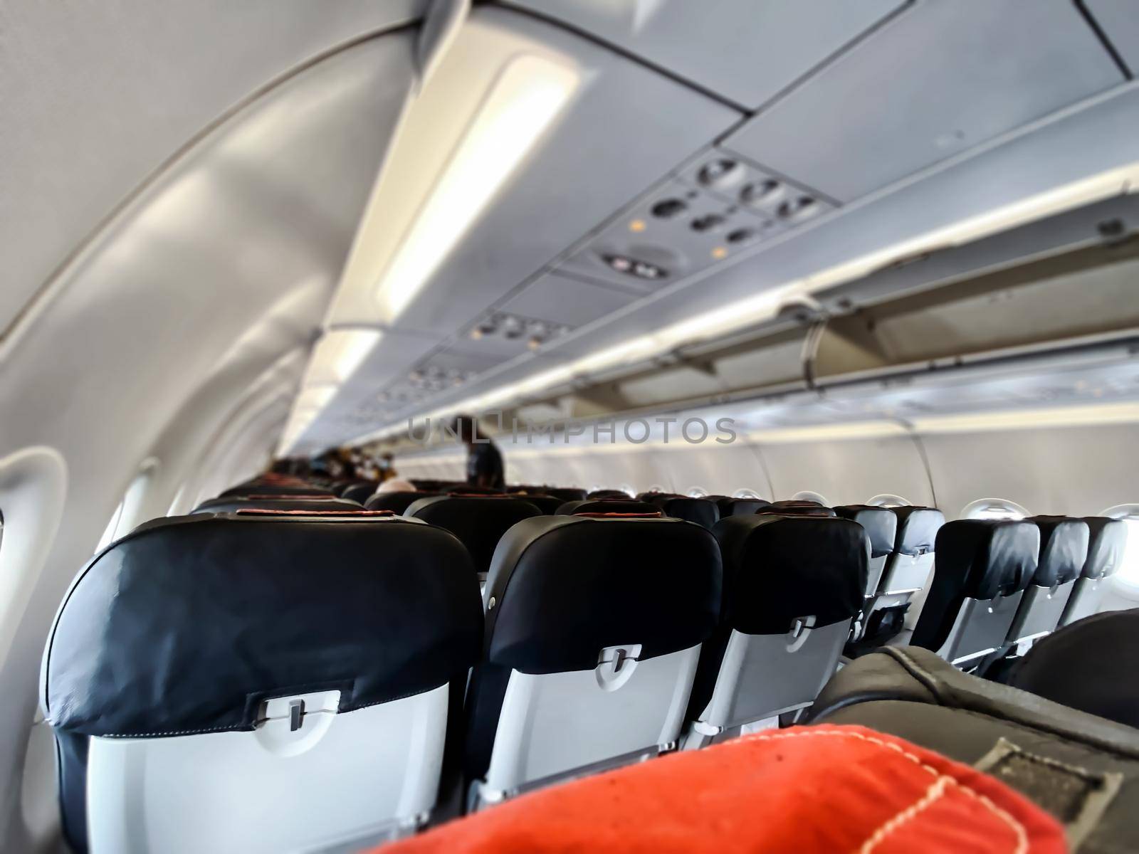 Interior of a cabin of a commercial airliner while some unrecognizable passengers are boarding. Rows of empty seats. Selective focus. Travel and transportation