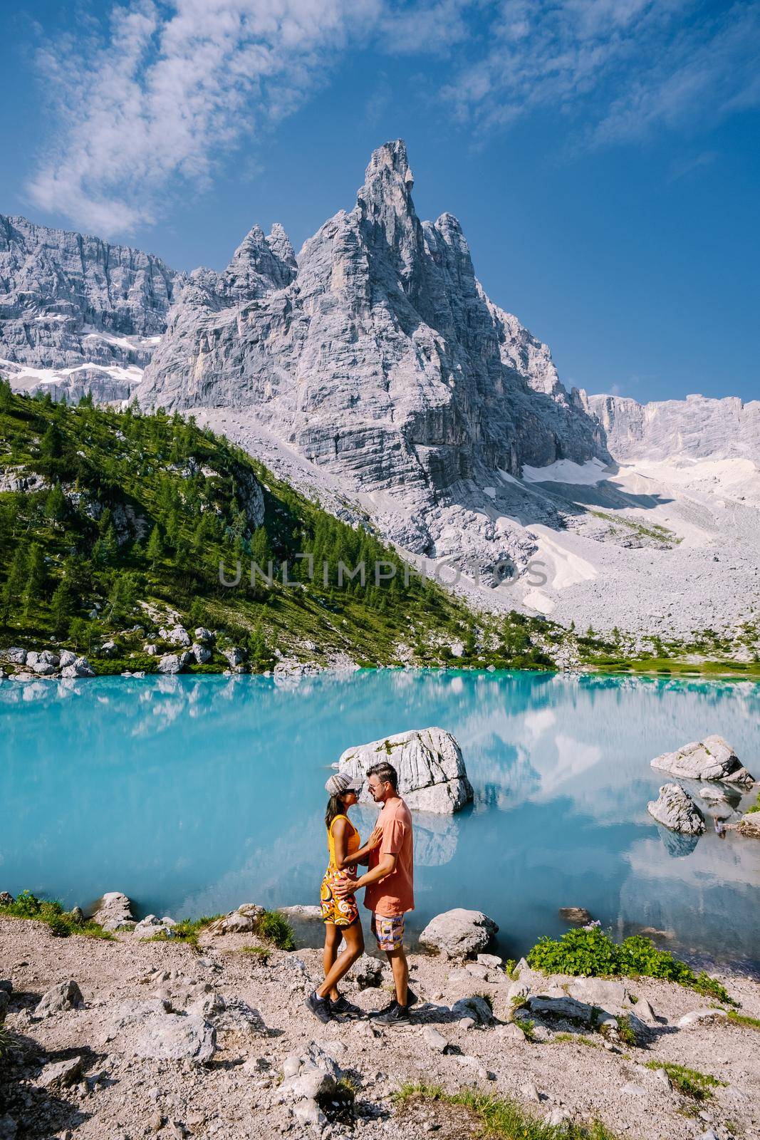 Morning with clear sky on Lago di Sorapis in the Italian Dolomites, milky blue lake Lago di Sorapis, Lake Sorapis, Dolomites, Italy. Couple man and woman mid age walking by the lake in the mountains 