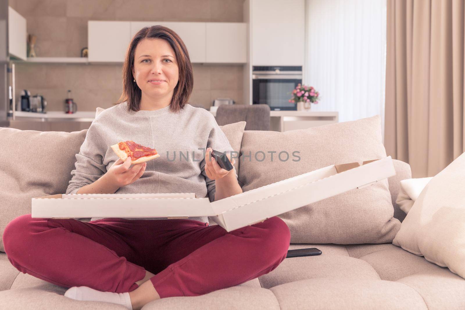 Beautiful woman eating pizza and watching TV holding remote control at home