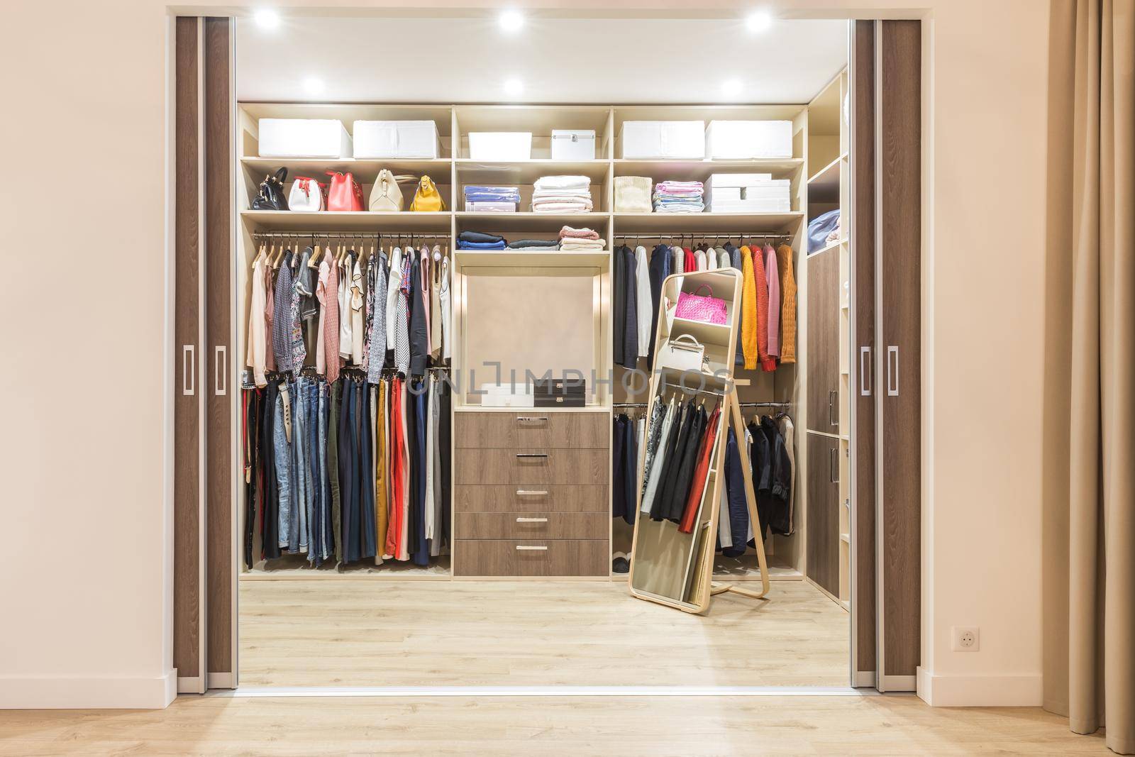Modern wooden wardrobe with clothes hanging on rail in walk in closet design interior