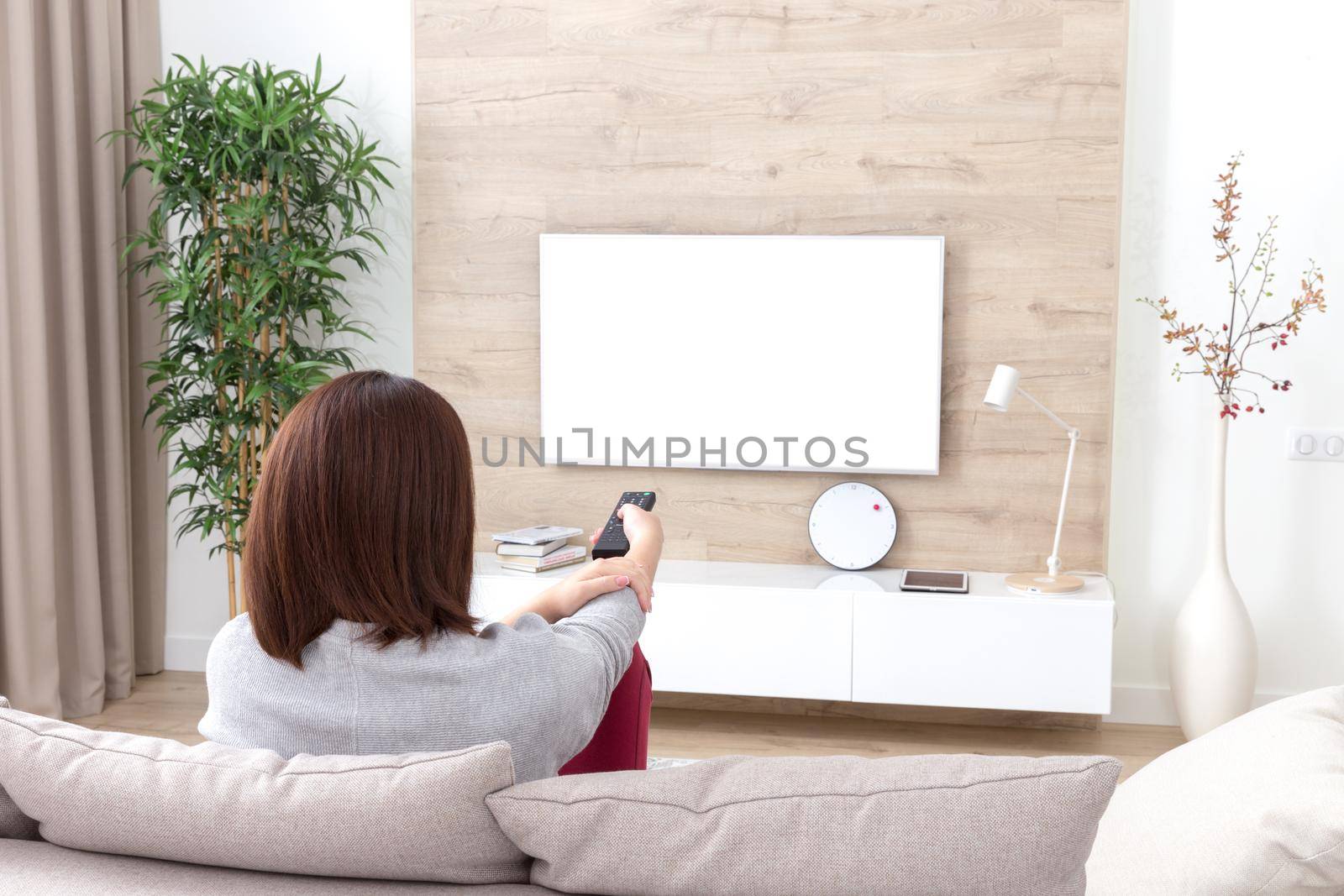 Young woman watching TV in the living room holding remote. white screen with copy space