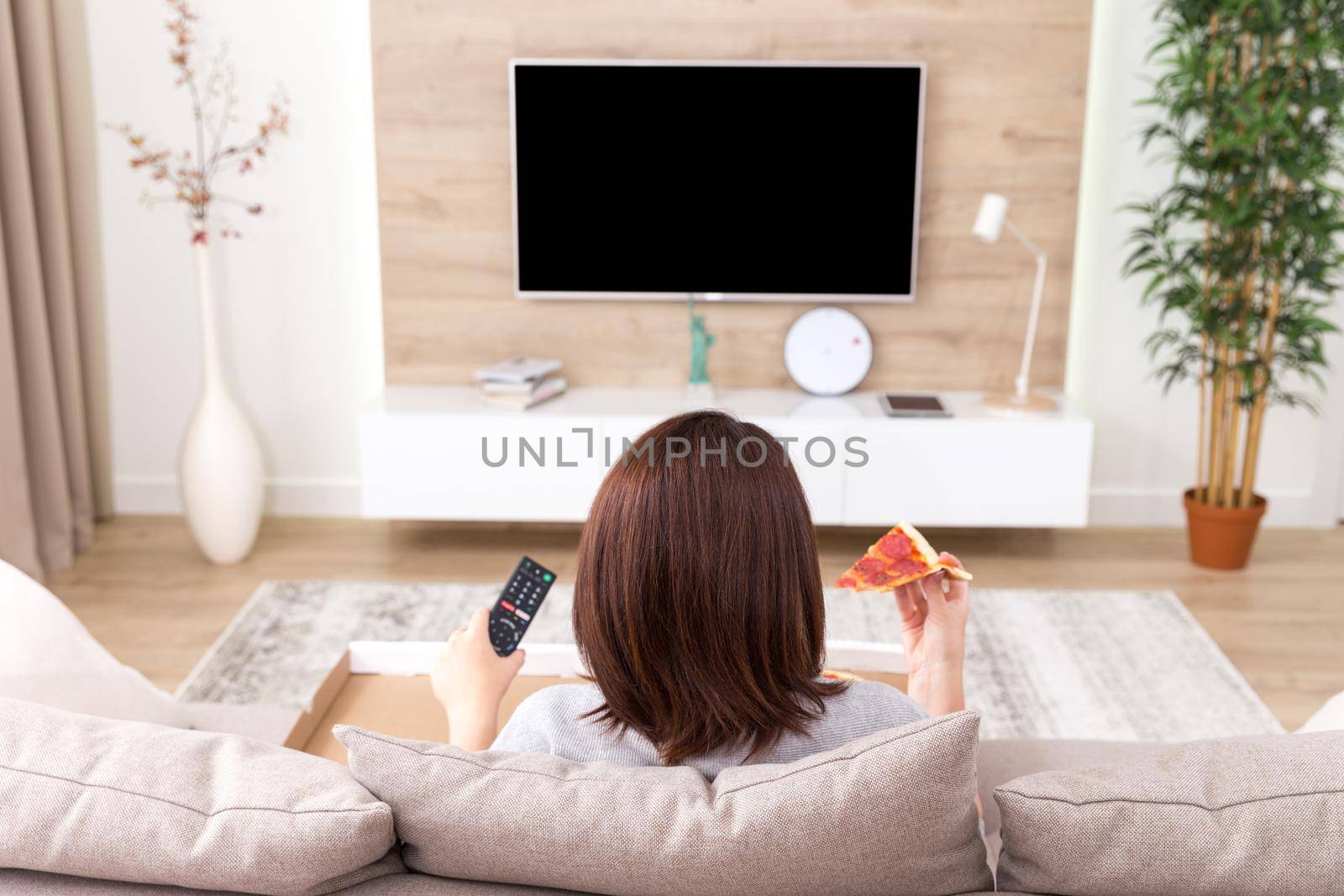 Single woman eating pizza and watching tv by Mariakray