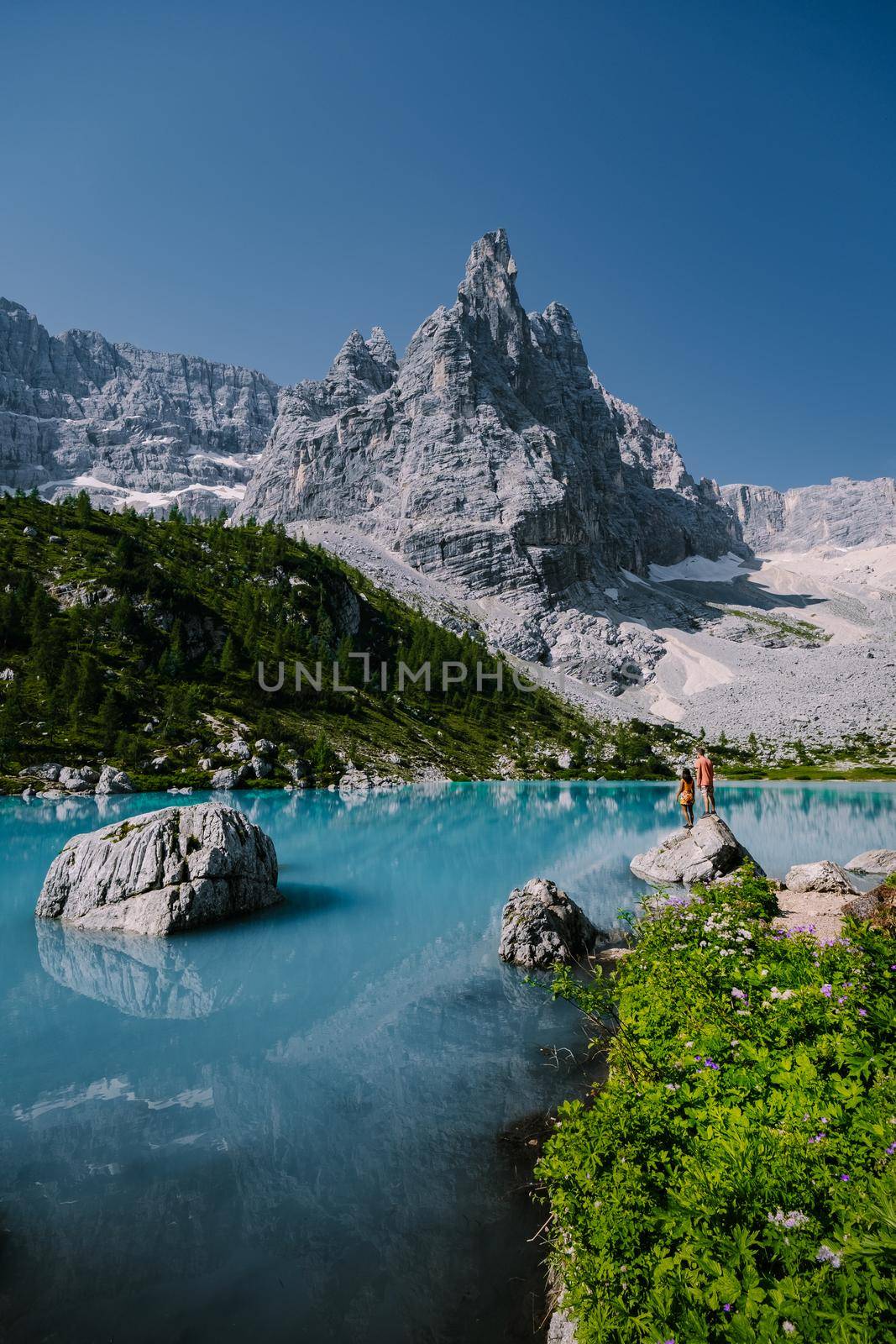 Morning with clear sky on Lago di Sorapis in the Italian Dolomites, milky blue lake Lago di Sorapis, Lake Sorapis, Dolomites, Italy. Couple man and woman mid age walking by the lake in the mountains 