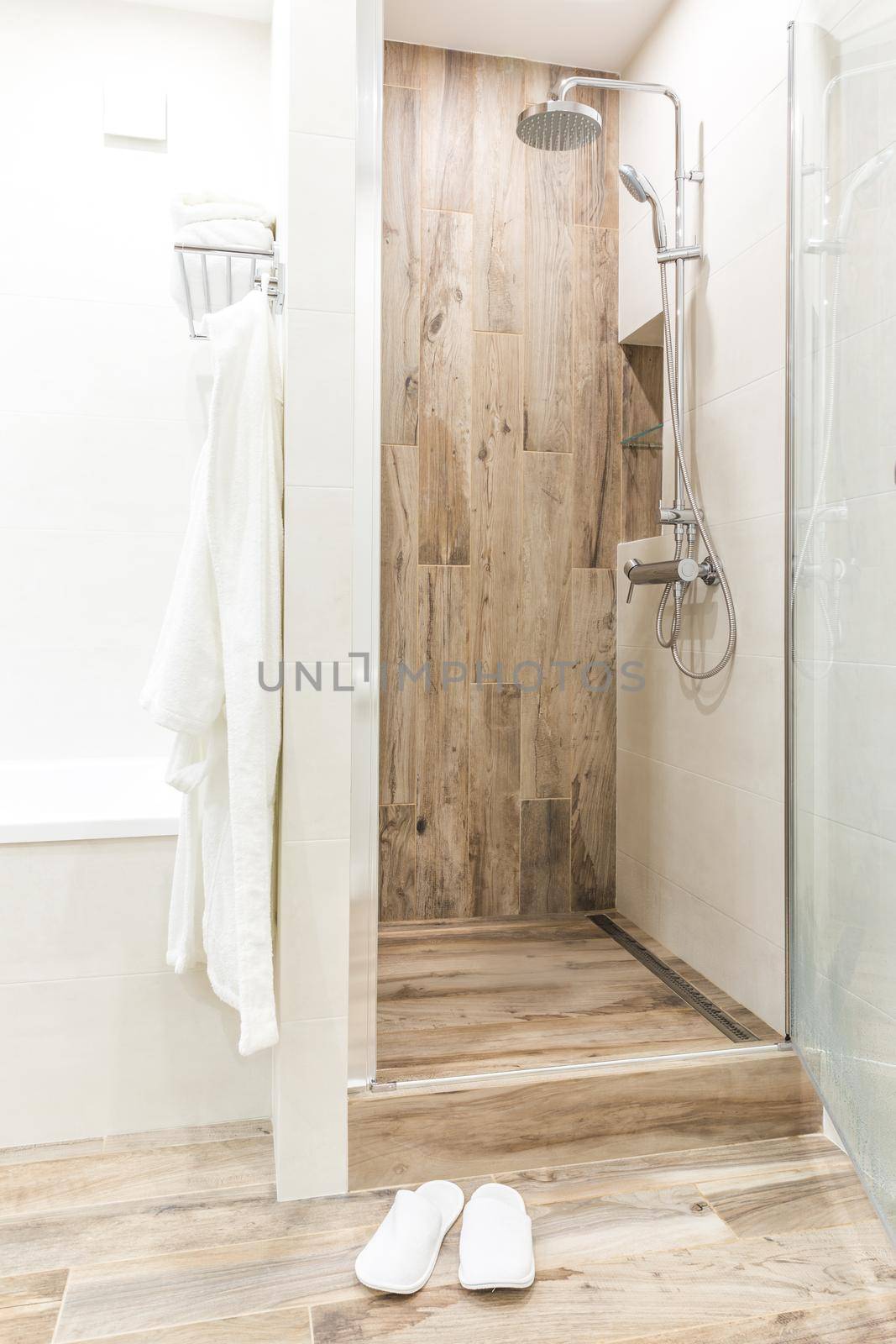 Walk in shower in bathroom with wooden style tile, glass door and hanging bathrobe