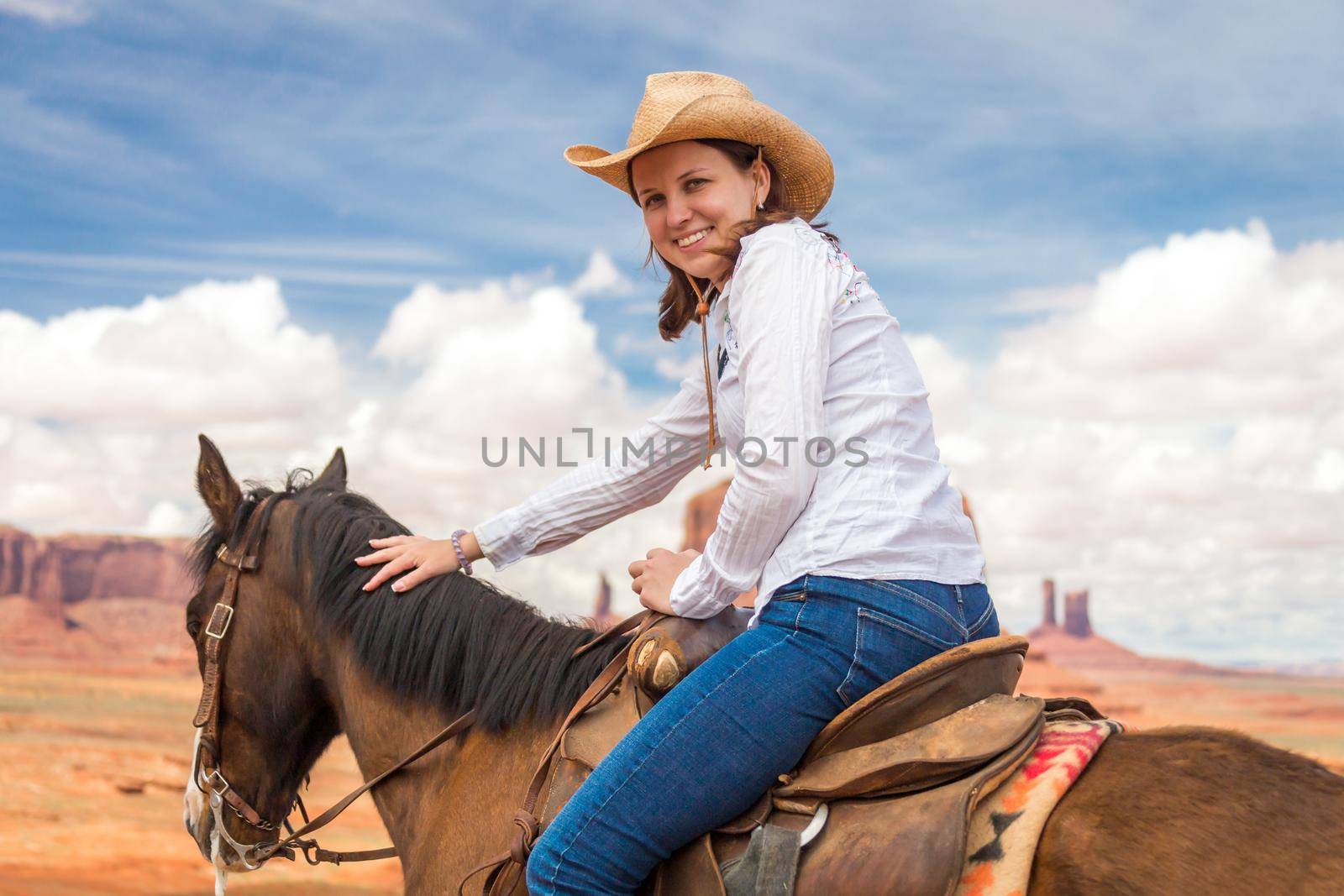 Cowgirl wearing straw hat riding horse in Monument Valley by Mariakray