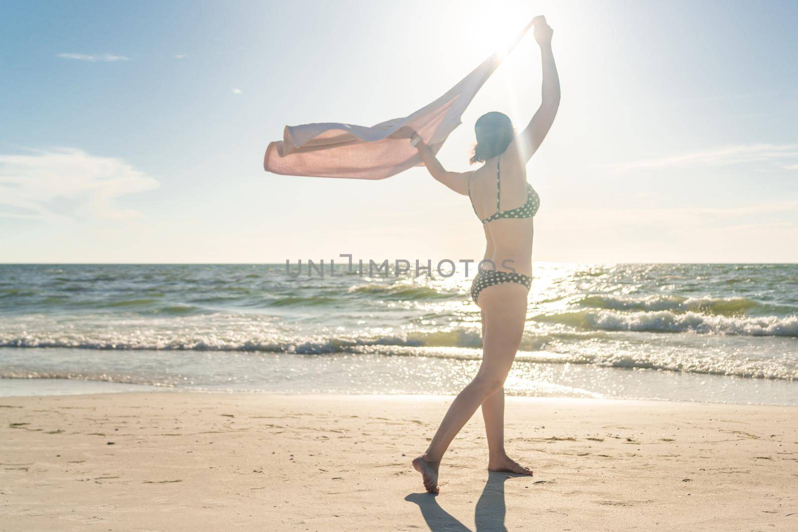 Woman standing with towel on the beach with ocean on background by Mariakray