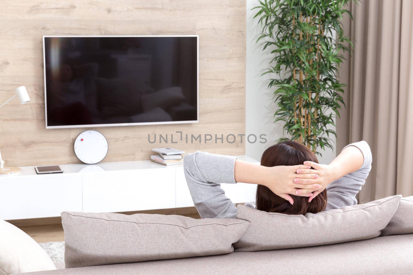 Young woman watching TV in the living room with arms crossed over head