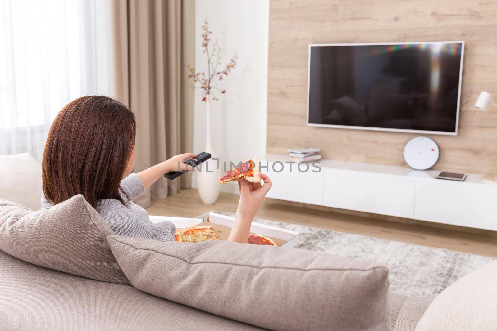Woman sitiing on couch eating pizza and watching tv