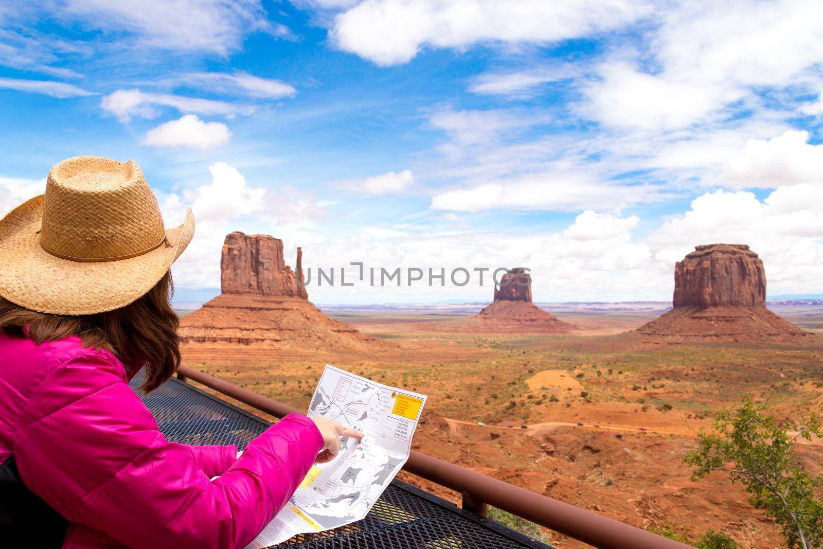 Back side of girl wearing straw hat searching right direction on map in Monument Valley, Utah, USA