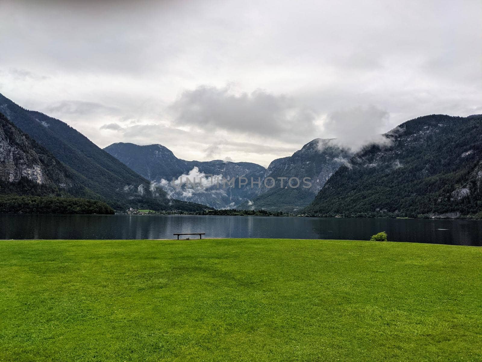 Alpine lake Hallstatter See during rain with a bench and green grass
