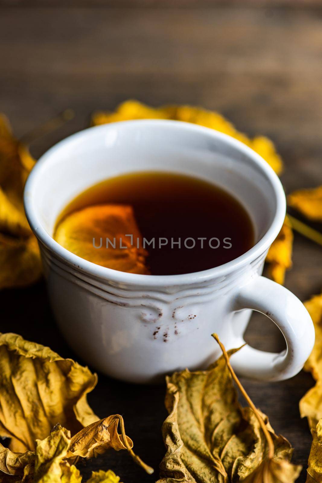 Cup of tea with lemon and dry leaves on wooden table