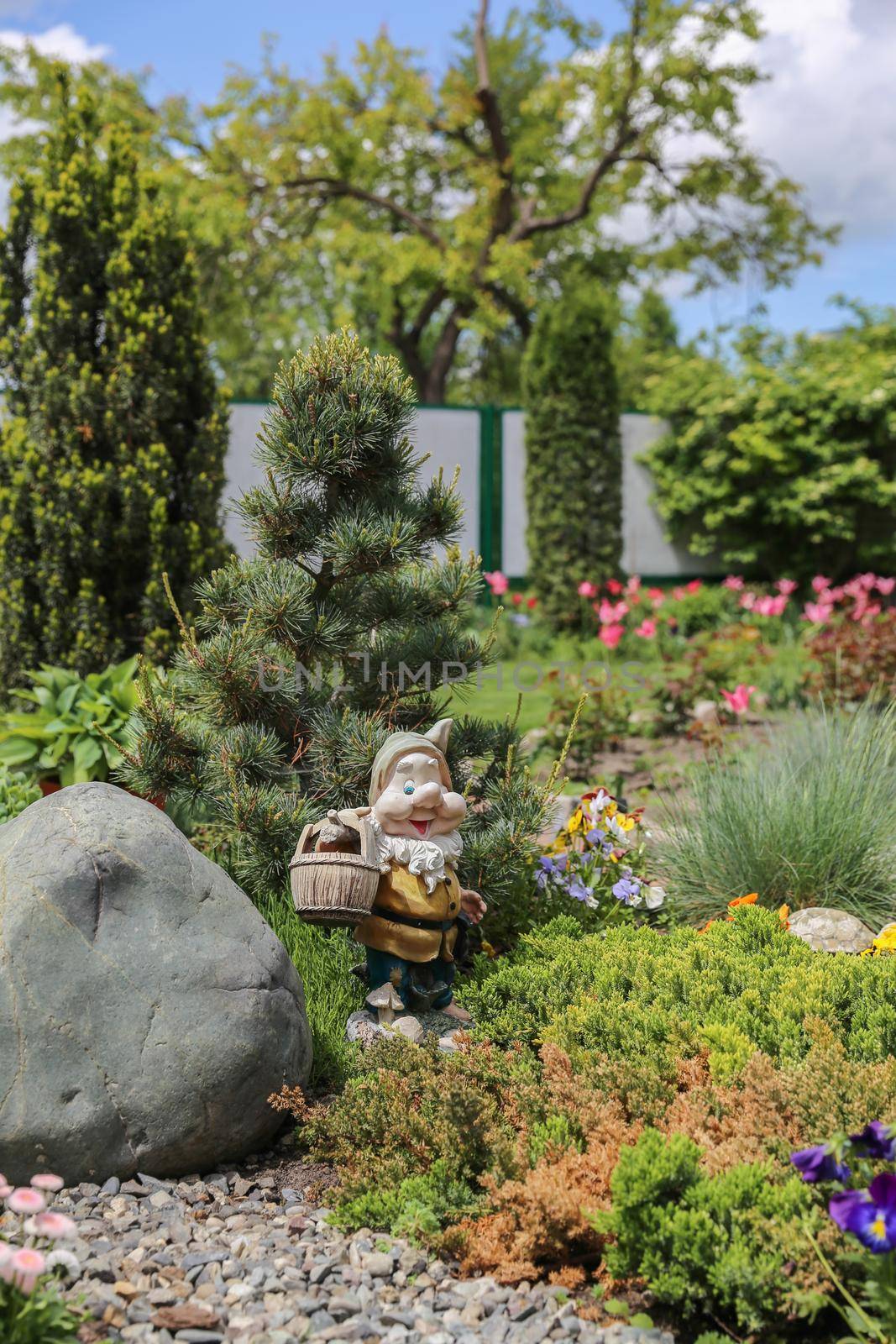 Funny garden gnome standing among nice flowers