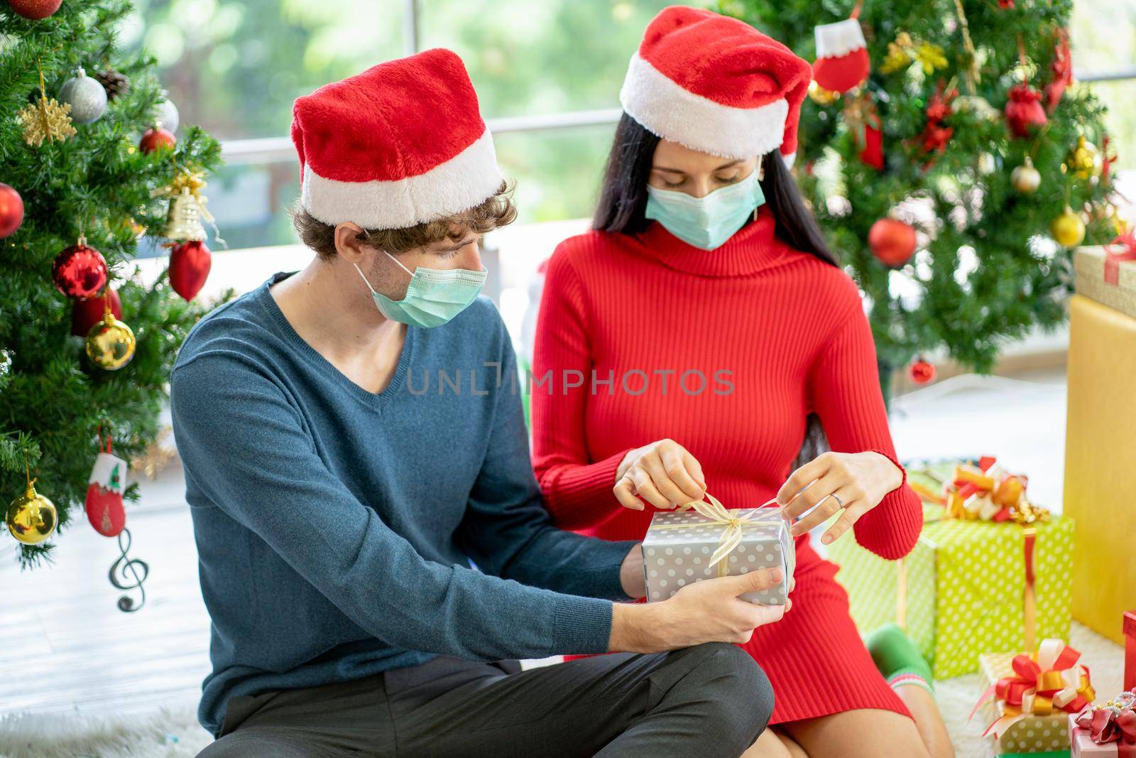Couple man and woman with hygiene mask help to prepare present or gift of Christmas festival together with new normal lifestyle to stay home during pandemic of Covid-19. by nrradmin