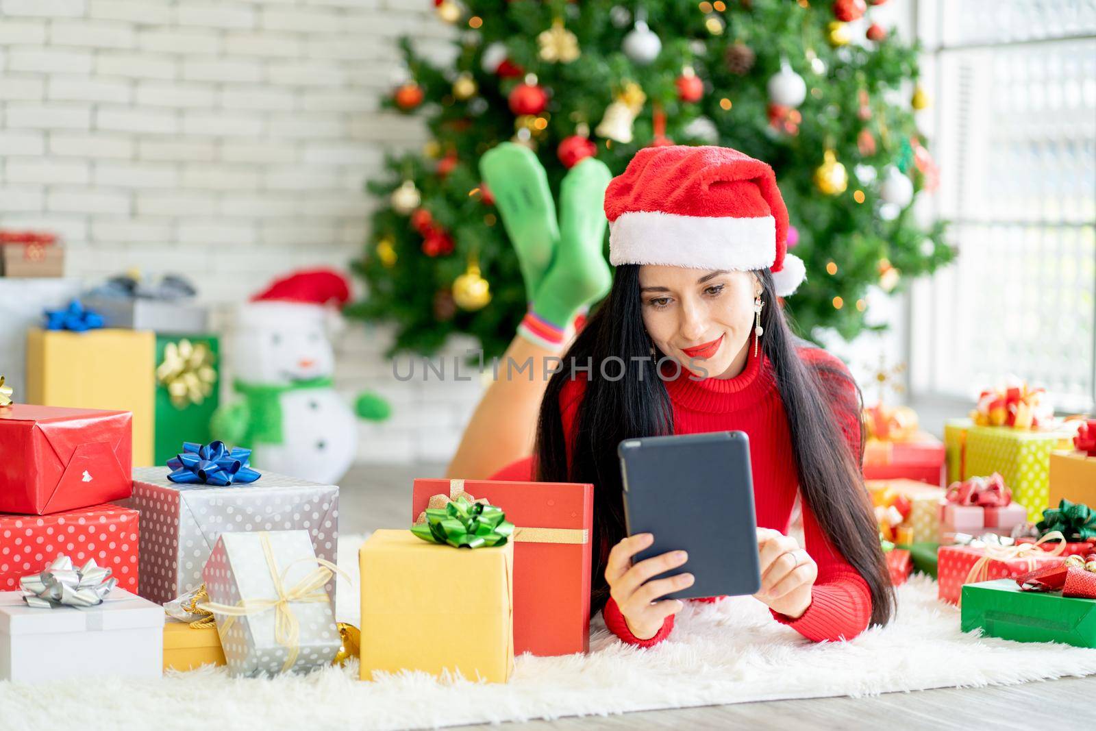 Pretty woman lie on floor among decoration of Christmas festival and she use tablet look like for online shopping with happiness.