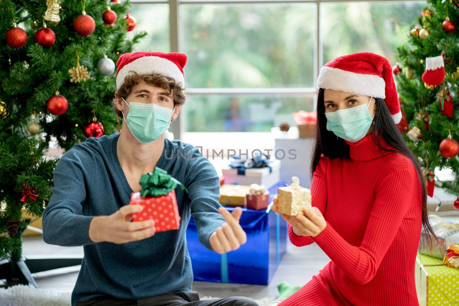 Couple man and woman with hygiene mask hold gift box and show to camera for Christmas festival during Covid-19 pandemic around the world. by nrradmin