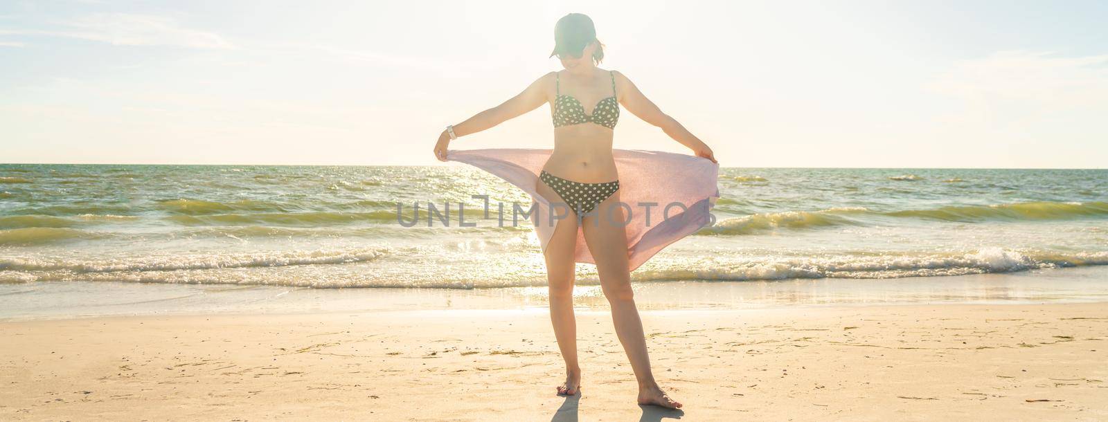 Woman standing with towel on the beach with ocean on background by Mariakray