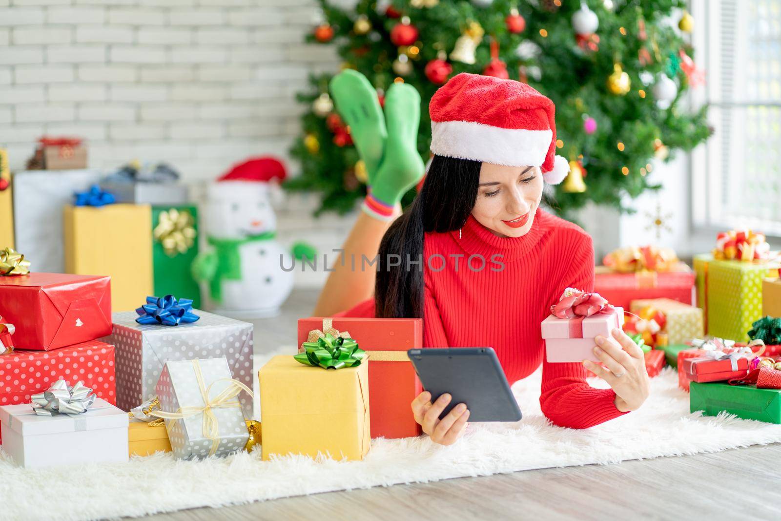 Woman with Christmas costume lie on floor of living room of her house and hold gift box and tablet look like online shopping. by nrradmin