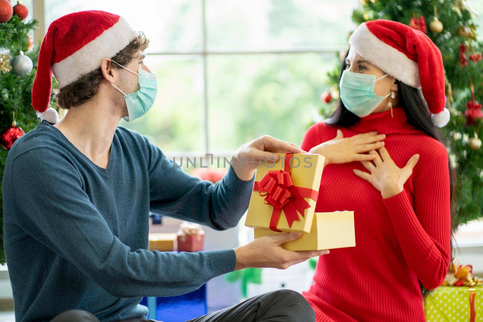 Caucasian man with hygiene mask show the present or gift to his couple woman and she action of surprise for Christmas celebration during pandemic of Covid-19 to stay at home of new normal lifestyle. by nrradmin
