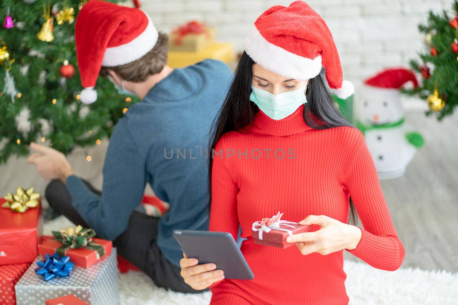 Caucasian woman with hygiene mask choose the gift from online shop and ask help from her couple for celebration of Christmas during Covid-19 pandemic and new normal lifestyle to stay at home. by nrradmin