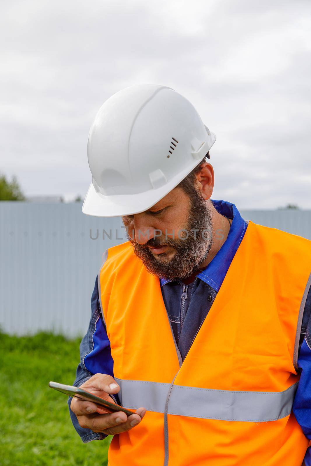 A civil engineer looks at a mobile phone. A bearded man is looking for information on his mobile phone.